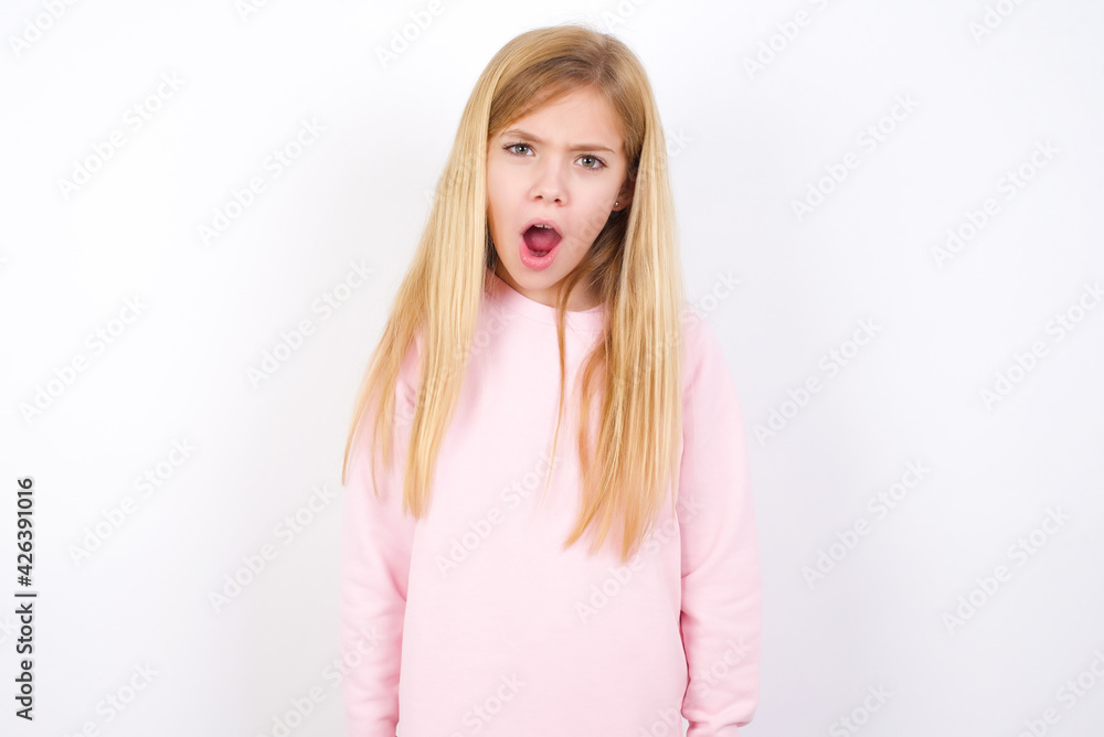 Expressive facial expressions. Shocked stupefied beautiful caucasian little girl wearing pink hoodie over white background, keeps jaw dropped feels stunned from what he sees aside. Expressive facial expressions. Shocked stupefied beautiful caucasian little girl wearing pink hoodie over white background, keeps jaw dropped feels stunned from what he sees aside.