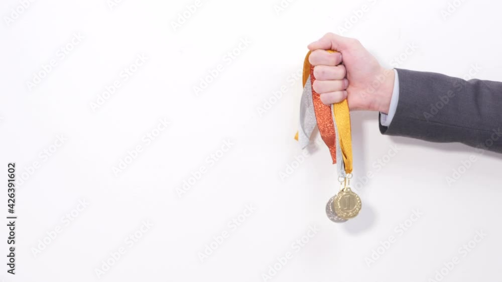 Male hand holds two medals golden and silver first and second place concept of victory best performance orange and yellow ribbons white background success in business. Close up 4K Ultra HD. Male hand holds two medals golden and silver first and second place concept of victory best performance orange and yellow ribbons white background success in business. Close up 4K Ultra HD.