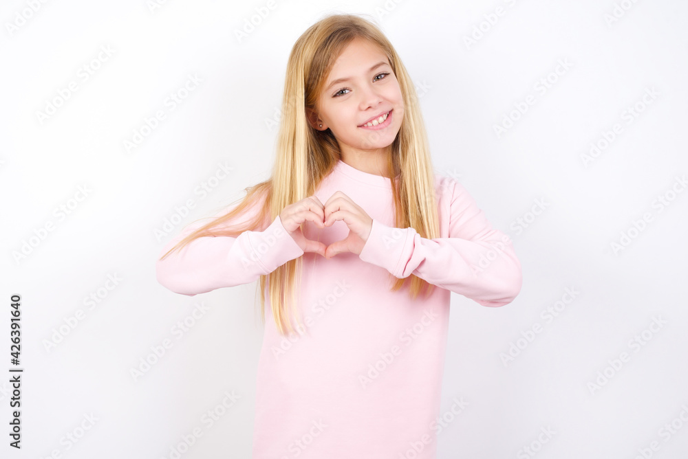 beautiful caucasian little girl wearing pink hoodie over white background smiling in love showing heart symbol and shape with hands. Romantic concept. beautiful caucasian little girl wearing pink hoodie over white background smiling in love showing heart symbol and shape with hands. Romantic concept.