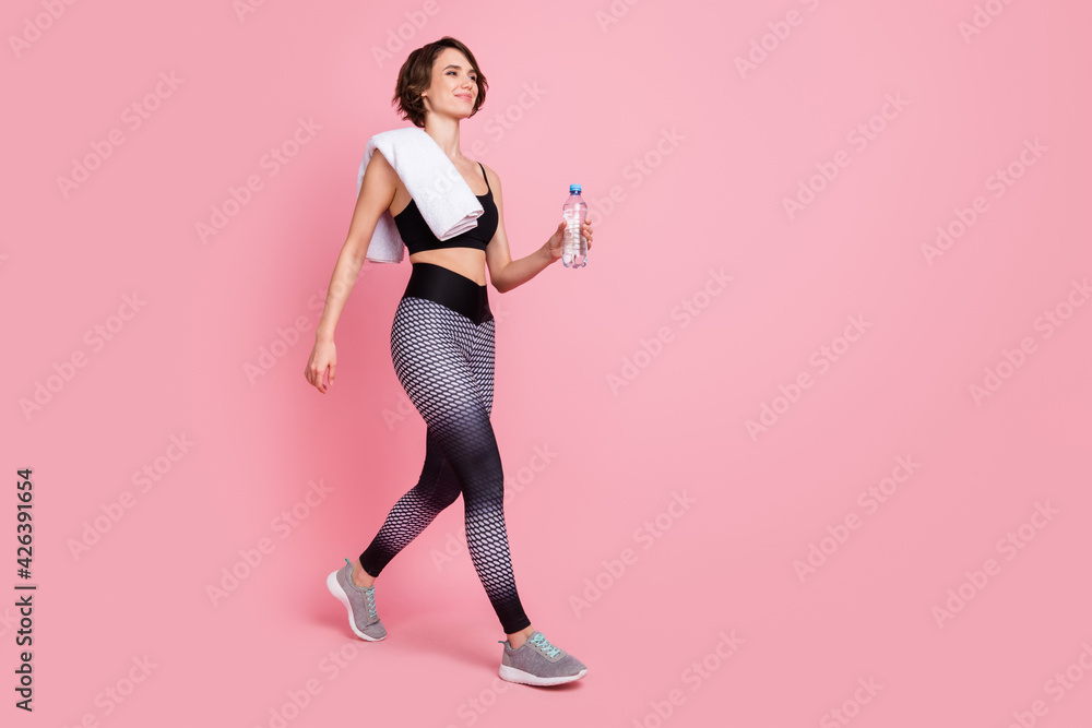 Full size profile side photo of brunette bob haired young woman walk hold bottle towel isolated on pink color background Full size profile side photo of brunette bob haired young woman walk hold bottle towel isolated on pink color background