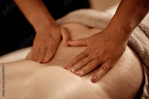 Close-up of the masseur hands on the back of a young woman. Wellness massage. Candlelight. The concept of alternative medicine. No face.