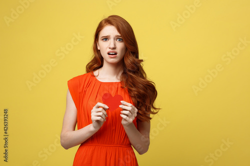 Attractive ginger girl holding paper heart and frowning, being nervous while confessing to her crush photo