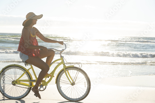 Happy mixed race woman on beach holiday riding bicycle on the sand by the sea