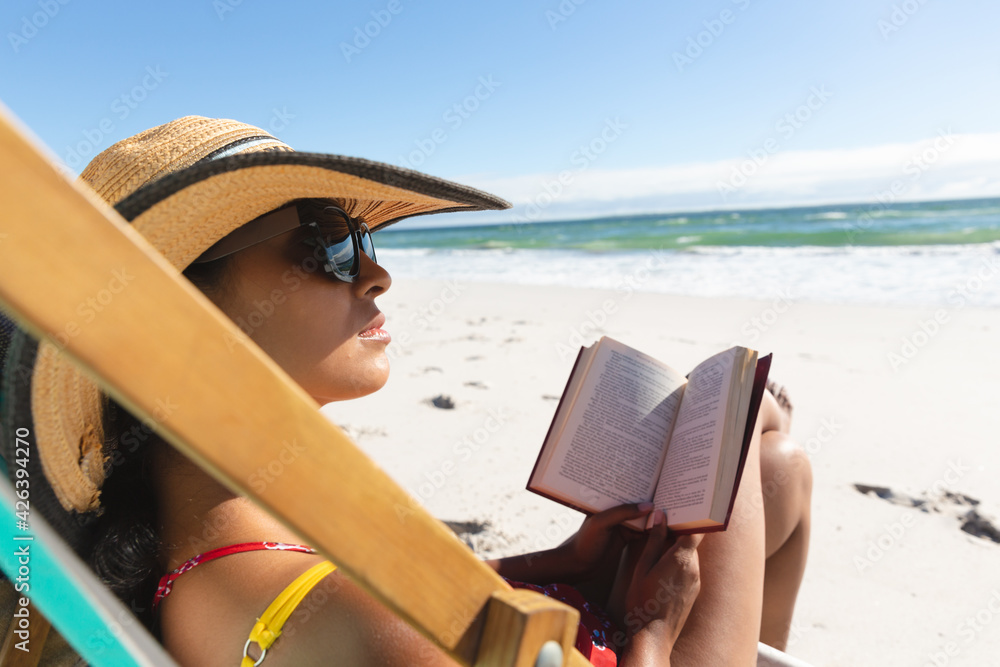 Mixed race woman on beach holiday sitting in deckchair reading book Mixed race woman on beach holiday sitting in deckchair reading book