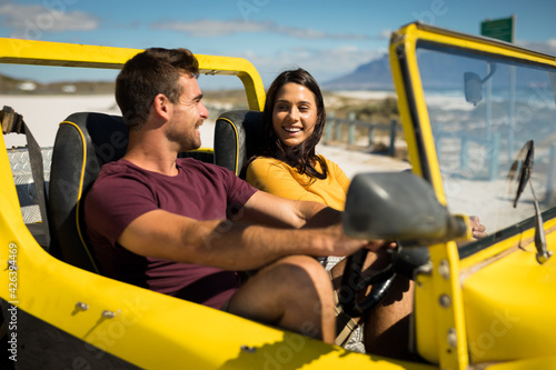 Happy caucasian couple sitting in beach buggy by the sea talking