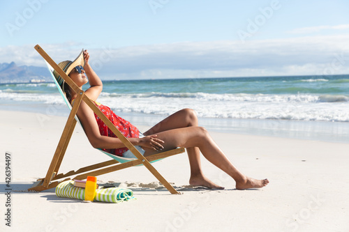 Mixed race woman on beach holiday sitting in deckchair sunbathing