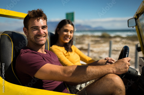 Portraits of happy caucasian couple looking to camera sitting in beach buggy by the sea talking