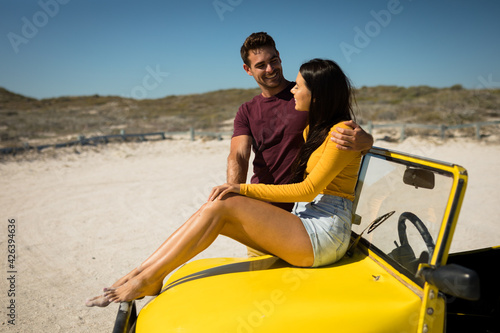 Happy caucasian couple by the sea smiling to each other, woman sitting on beach buggy