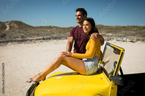 Happy caucasian couple, man embracing woman sitting on beach buggy by the sea