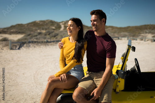 Happy caucasian couple sitting on beach buggy by the sea smiling