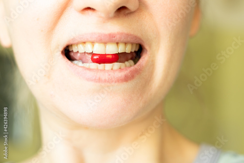 Girl holds vitamin red in her mouth  close-up
