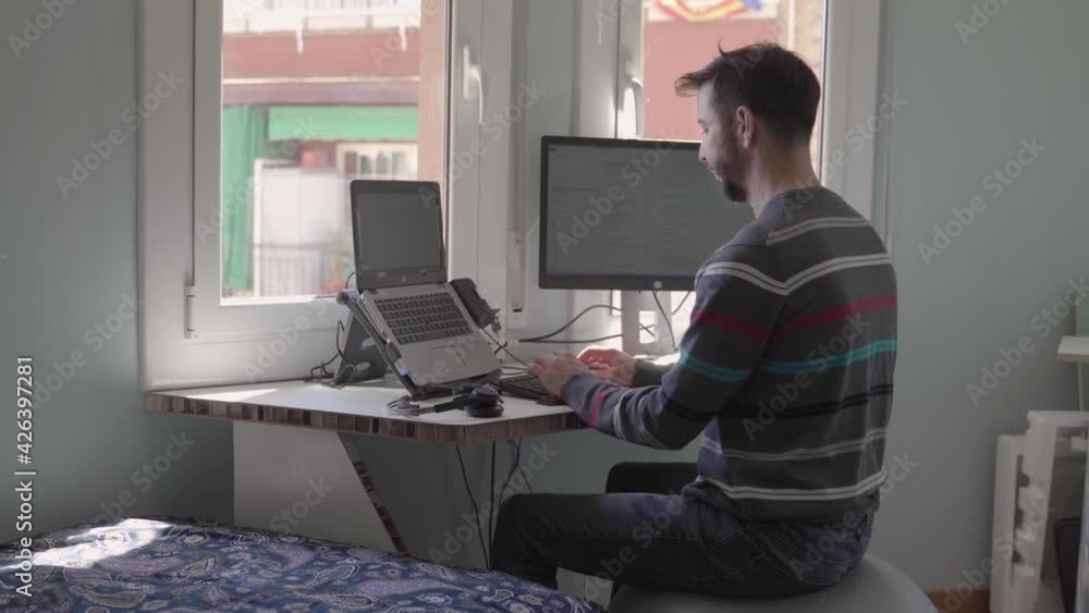 Young Man working remotely with laptop from home. Guy working online from his tiny bedroom in times of covid cornavirus pandemic new normal Young Man working remotely with laptop from home. Guy working online from his tiny bedroom in times of covid cornavirus pandemic new normal
