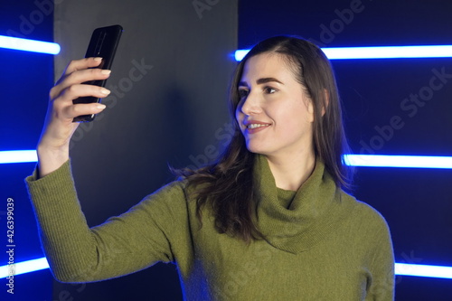 Girl takes selfie on phone against background with neon lights photo