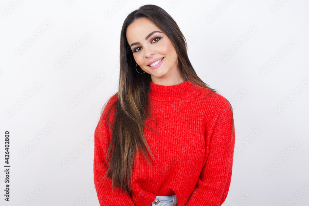 Fototapeta premium Unhappy young beautiful brunette woman wearing red knitted sweater over white wall crying while posing at camera whipping tears with hand.
