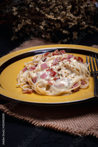 Carbonara spaghetti with ham  sprinkle oregano in a yellow plate on a black table.