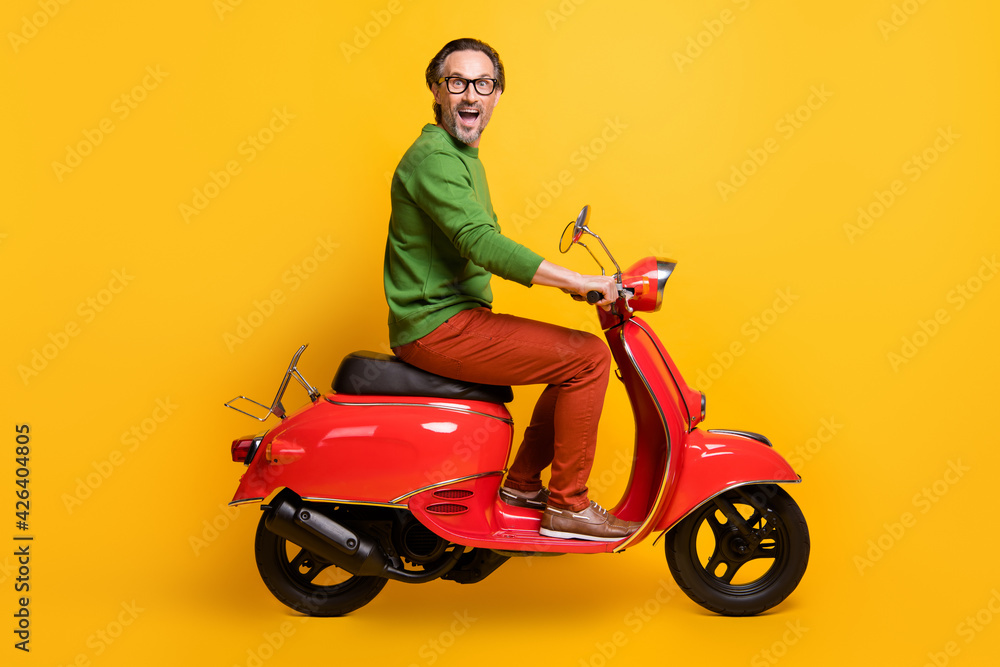 Photo of excited man ride scooter open mouth wear glasses green sweater pants shoes isolated yellow color background Photo of excited man ride scooter open mouth wear glasses green sweater pants shoes isolated yellow color background