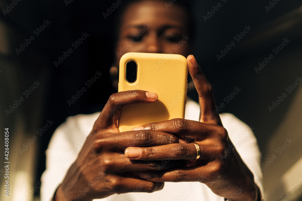 view from below of an afro or black girl's hands with a cell phone. American woman communicating with her smartphone. Hands of young black girl holding a phone. - obrazy, fototapety, plakaty 