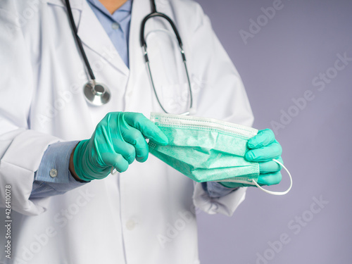 Close-up of hands doctor wearing gloves and holding a face mask while standing on gray background. Space for text. Concept of healthcare