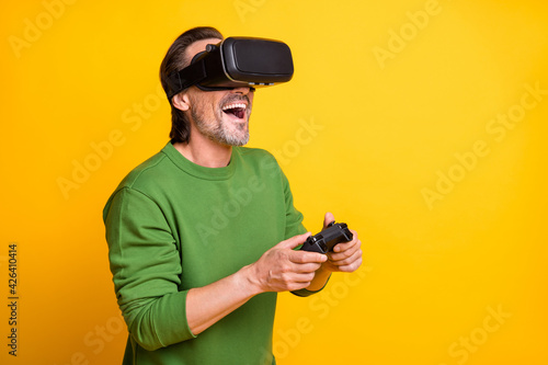 Photo portrait of bearded man keeping video game console playing in vr glasses smiling isolated on vibrant yellow color background