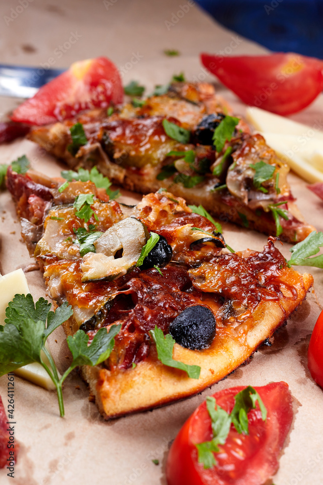 Two slice of pizza with olives, eggplant, salami and tomatoes