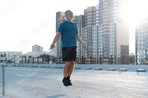 Middle-aged man exercising with jump-rope outdoors.