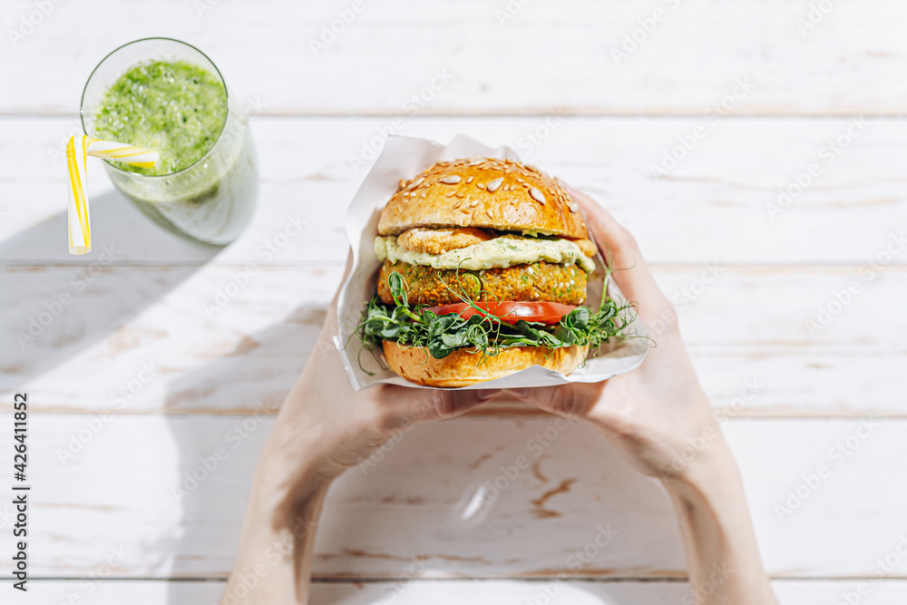 Vegan with a lump, gluten-free, with flax seeds. chickpea burgers with arugula, radish, avocado cucumber and hummus. Plant based diet concept. Burger in the hands of a woman sitting an open-air cafe