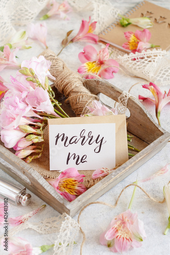 MARRY ME card on a white table between pink flowers photo