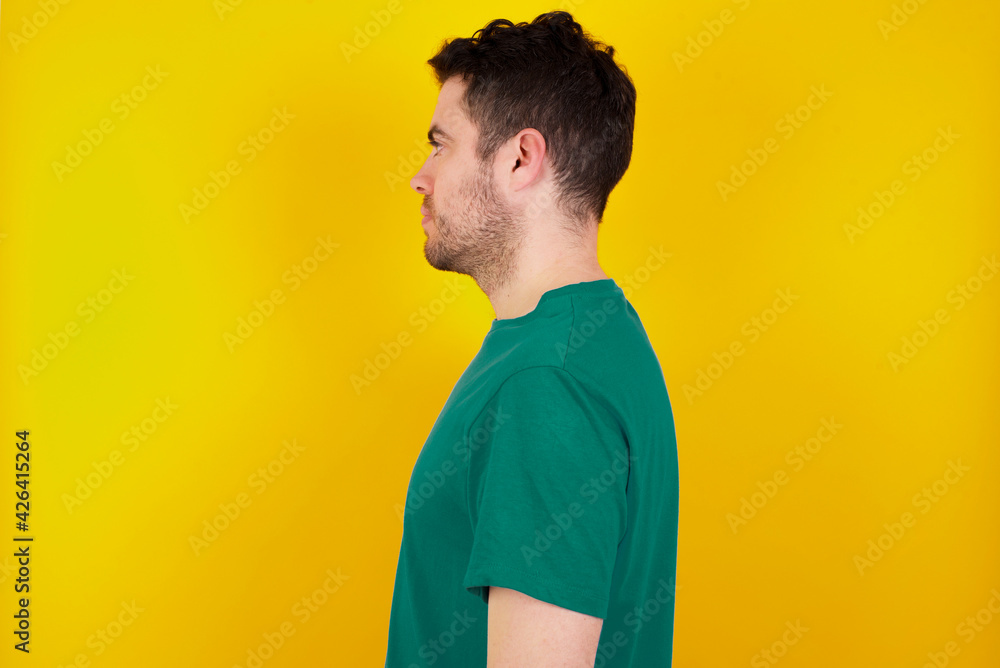 young Caucasian man wearing green T-shirt against yellow wall looking to side, relax profile pose with natural face with confident smile.