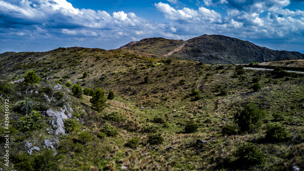 Obraz premium Las montañas mas altas, con las nubes pasando sobre ellas y el camino bordeando la base de la montaña hasta el horizonte. Cerro Champaqui. Merlo. Córdoba. Argentina