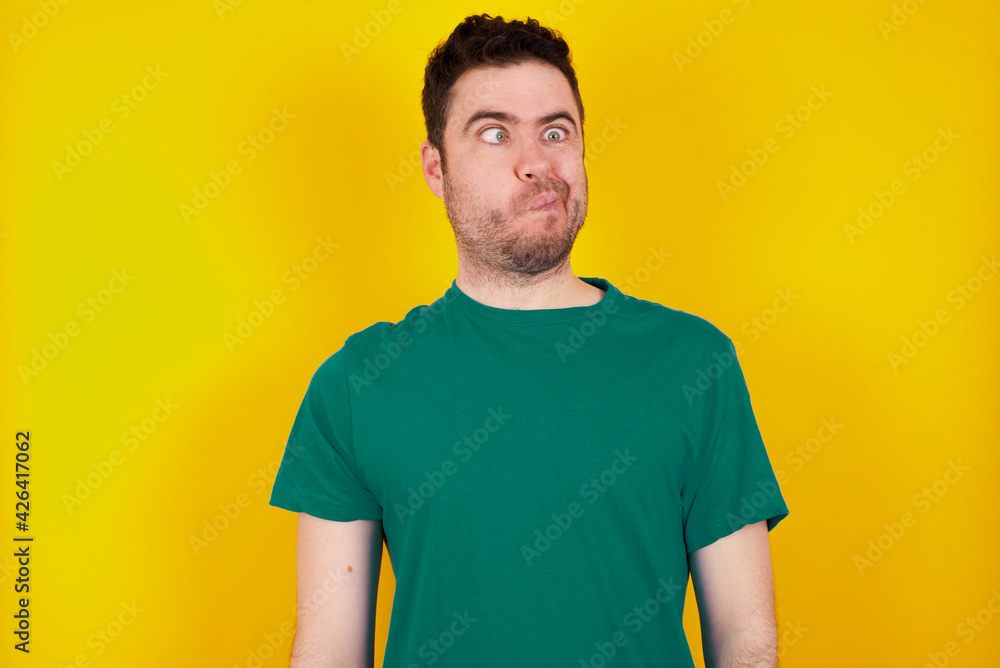 young Caucasian man wearing green T-shirt against yellow wall making grimace and crazy face, screaming out of control, funny lunatic expressing freedom and wild. young Caucasian man wearing green T-shirt against yellow wall making grimace and crazy face, screaming out of control, funny lunatic expressing freedom and wild.