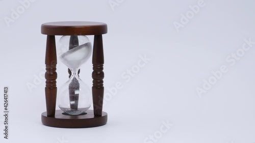 Sand trickle down in hourglass,Sand going through bulbs of hourglass, device used to measure passage of time, isolated oject, sand watch in three legged wooden stand. Close up, 4K Ultra HD. photo