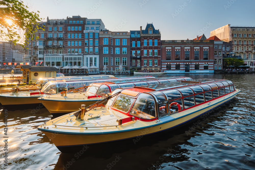 Tourist boats moored in Amsterdam canal pier on sunset