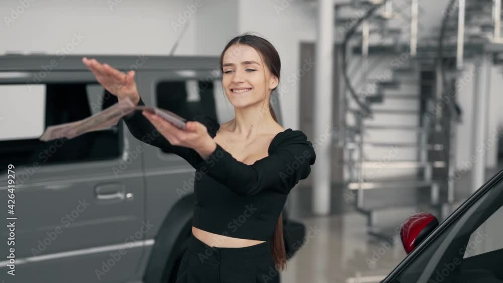 Happy young woman scattering money in a car dealership Happy young woman scattering money in a car dealership
