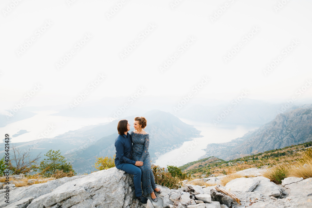 The bride and groom sitting embracing on the Lovcen mountain behind them opens a view of the Bay of Kotor 