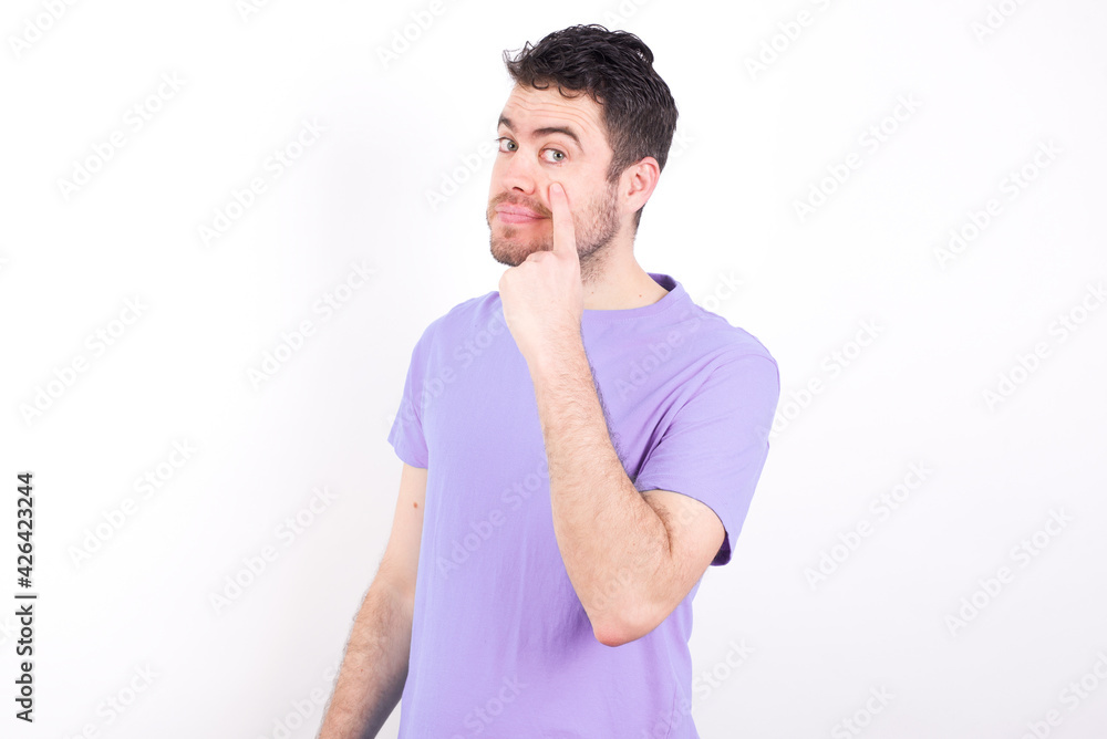 young handsome caucasian man wearing purple t-shirt against white background , looking, observing, keeping an eye on an object in front, or watching out for something. young handsome caucasian man wearing purple t-shirt against white background , looking, observing, keeping an eye on an object in front, or watching out for something.