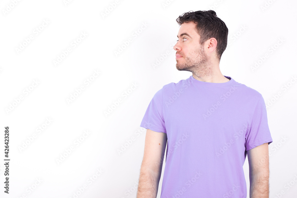 Side view of young happy smiling young handsome caucasian man wearing purple t-shirt against white background Side view of young happy smiling young handsome caucasian man wearing purple t-shirt against white background