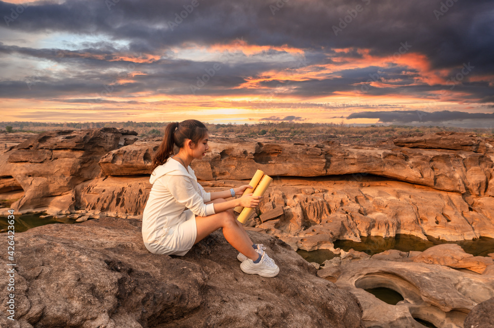 Beautiful young asian woman traveler sitting and looking at paper map on rock cliff in grand canyon of Thailand