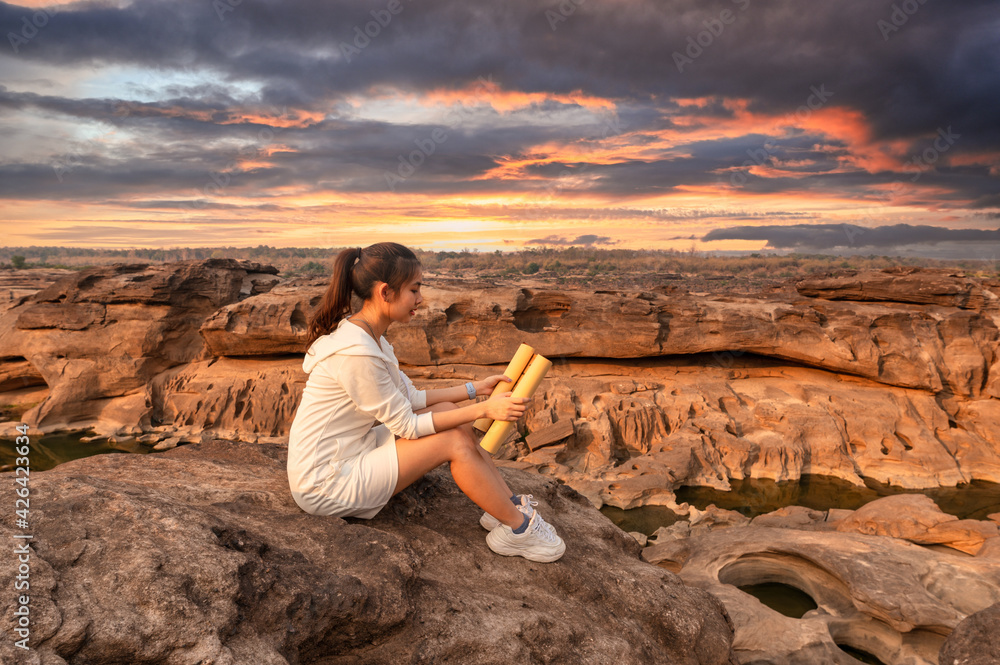 Beautiful young asian woman traveler sitting and looking at paper map on rock cliff in grand canyon of Thailand Beautiful young asian woman traveler sitting and looking at paper map on rock cliff in grand canyon of Thailand