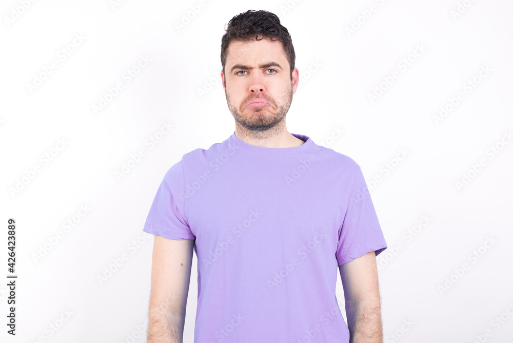 young handsome caucasian man wearing purple t-shirt against white wall crying desperate and depressed with tears on his eyes suffering pain and depression. Sad facial expression and emotion concept. young handsome caucasian man wearing purple t-shirt against white wall crying desperate and depressed with tears on his eyes suffering pain and depression. Sad facial expression and emotion concept.