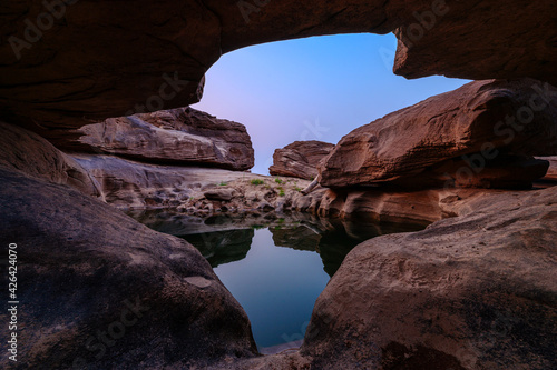 Geological hole cave in large rocky rapids and pond reflection in the evening