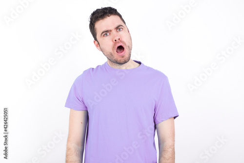 Expressive facial expressions. Shocked stupefied young handsome caucasian man wearing purple t-shirt against white background , keeps jaw dropped feels stunned from what he sees aside.