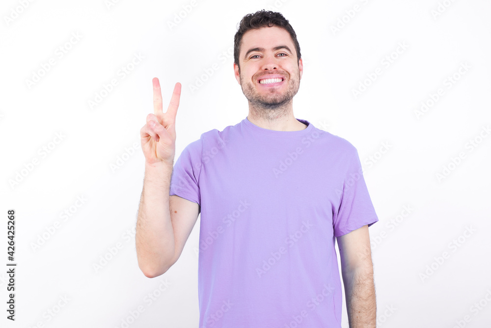young handsome caucasian man wearing purple t-shirt against white background showing and pointing up with fingers number two while smiling confident and happy. young handsome caucasian man wearing purple t-shirt against white background showing and pointing up with fingers number two while smiling confident and happy.