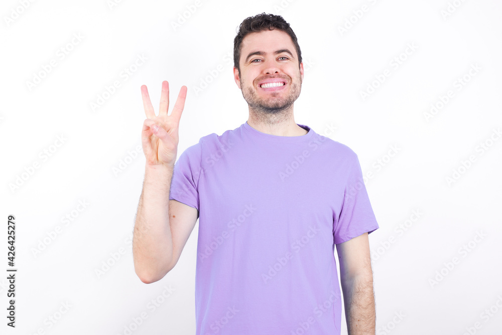 young handsome caucasian man wearing purple t-shirt against white background showing and pointing up with fingers number three while smiling confident and happy. young handsome caucasian man wearing purple t-shirt against white background showing and pointing up with fingers number three while smiling confident and happy.