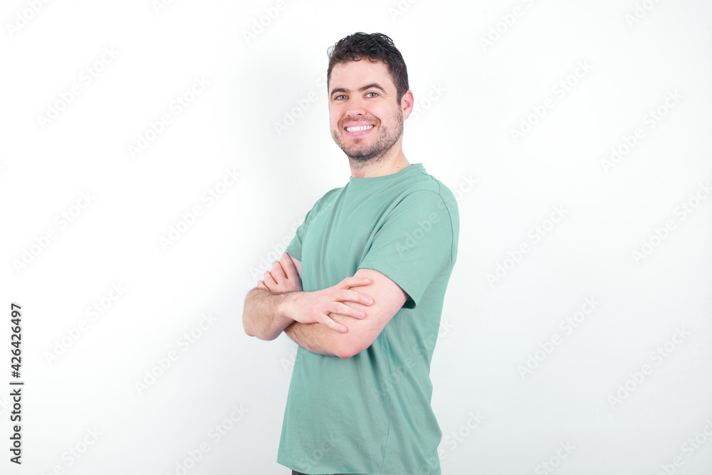 Image of cheerful young handsome caucasian man wearing green t-shirt against white background with arms crossed. Looking and smiling at the camera. Confidence concept. Image of cheerful young handsome caucasian man wearing green t-shirt against white background with arms crossed. Looking and smiling at the camera. Confidence concept.