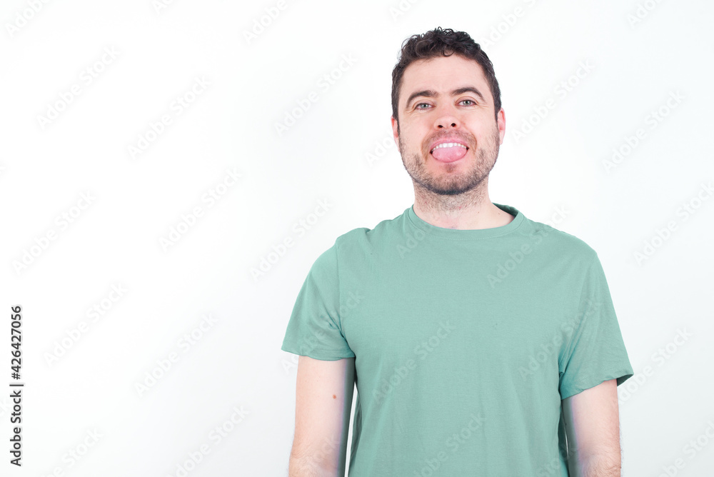 young handsome caucasian man wearing green t-shirt against white background with happy and funny face smiling and showing tongue. young handsome caucasian man wearing green t-shirt against white background with happy and funny face smiling and showing tongue.