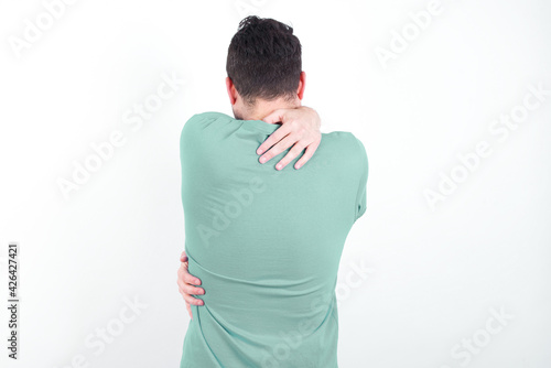 young handsome caucasian man wearing green t-shirt against white background hugging oneself happy and positive from backwards. Self love and self care.