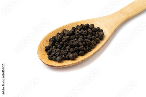 Closeup of black pepper grains on a wooden spoon isolated over white background