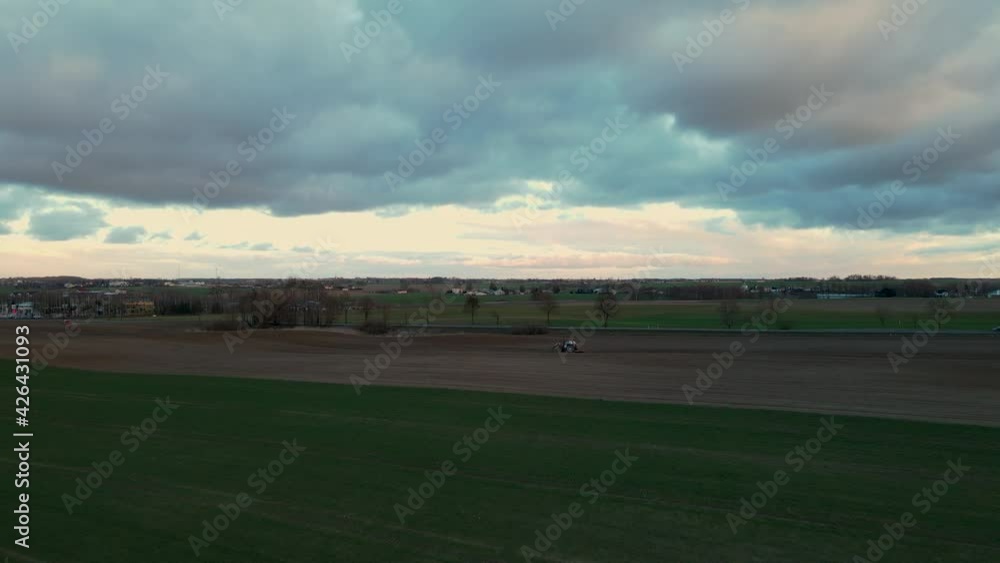 Farm Tractor Cultivating Land In Lubawa, Poland On A Cloudy Morning. aerial drone Farm Tractor Cultivating Land In Lubawa, Poland On A Cloudy Morning. aerial drone