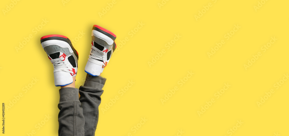 Close up of kids feet in a pair of colorful red sneakers isolated on yellow background. web border of sports and active leisure