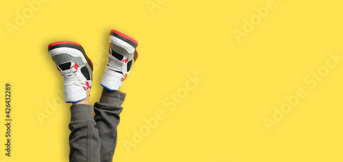 Obraz na płótnie Close up of kids feet in a pair of colorful red sneakers isolated on yellow background. web border of sports and active leisure w salonie